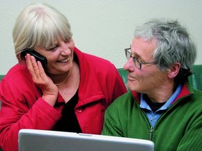 [Translate to Poland - Polish:] Elderly couple on front f a laptop looking at each other while she is talking on the phone