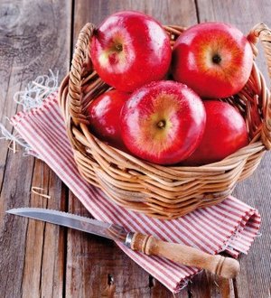 Red organic apples in a straw basket on wooden background jabłka